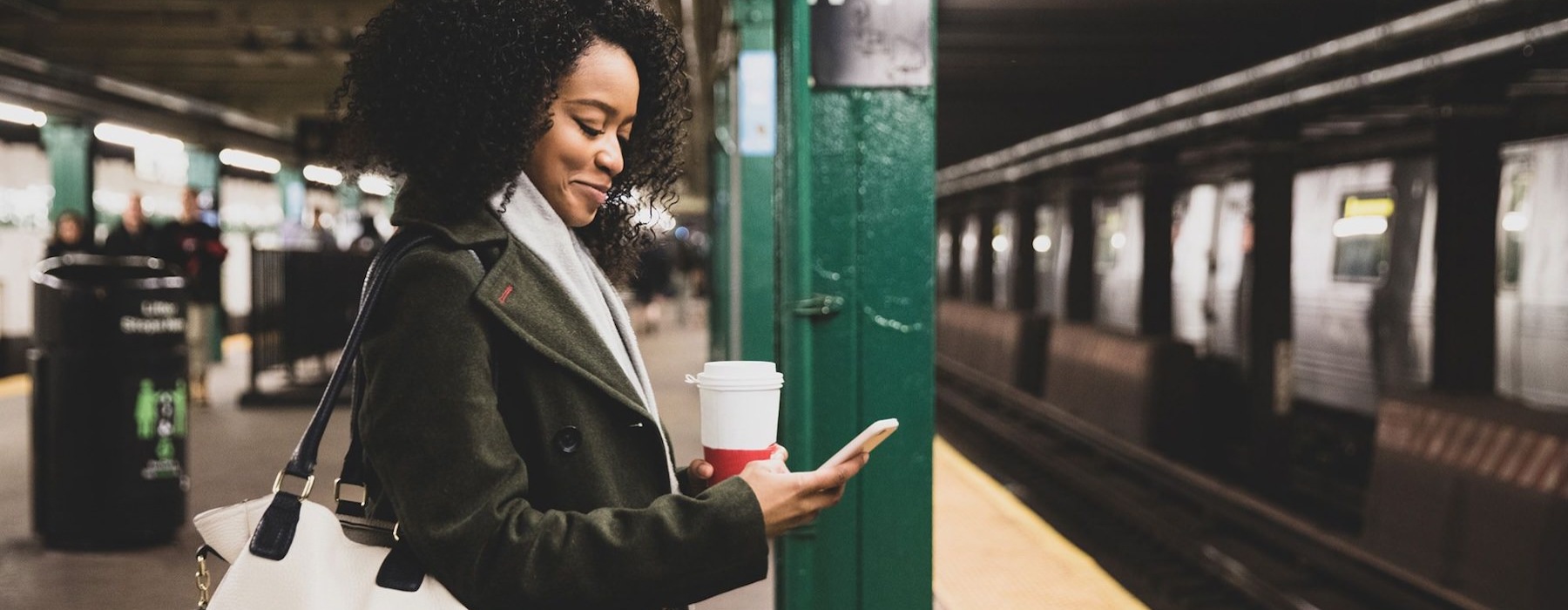 woman with a cup of coffee texts on subway station platform